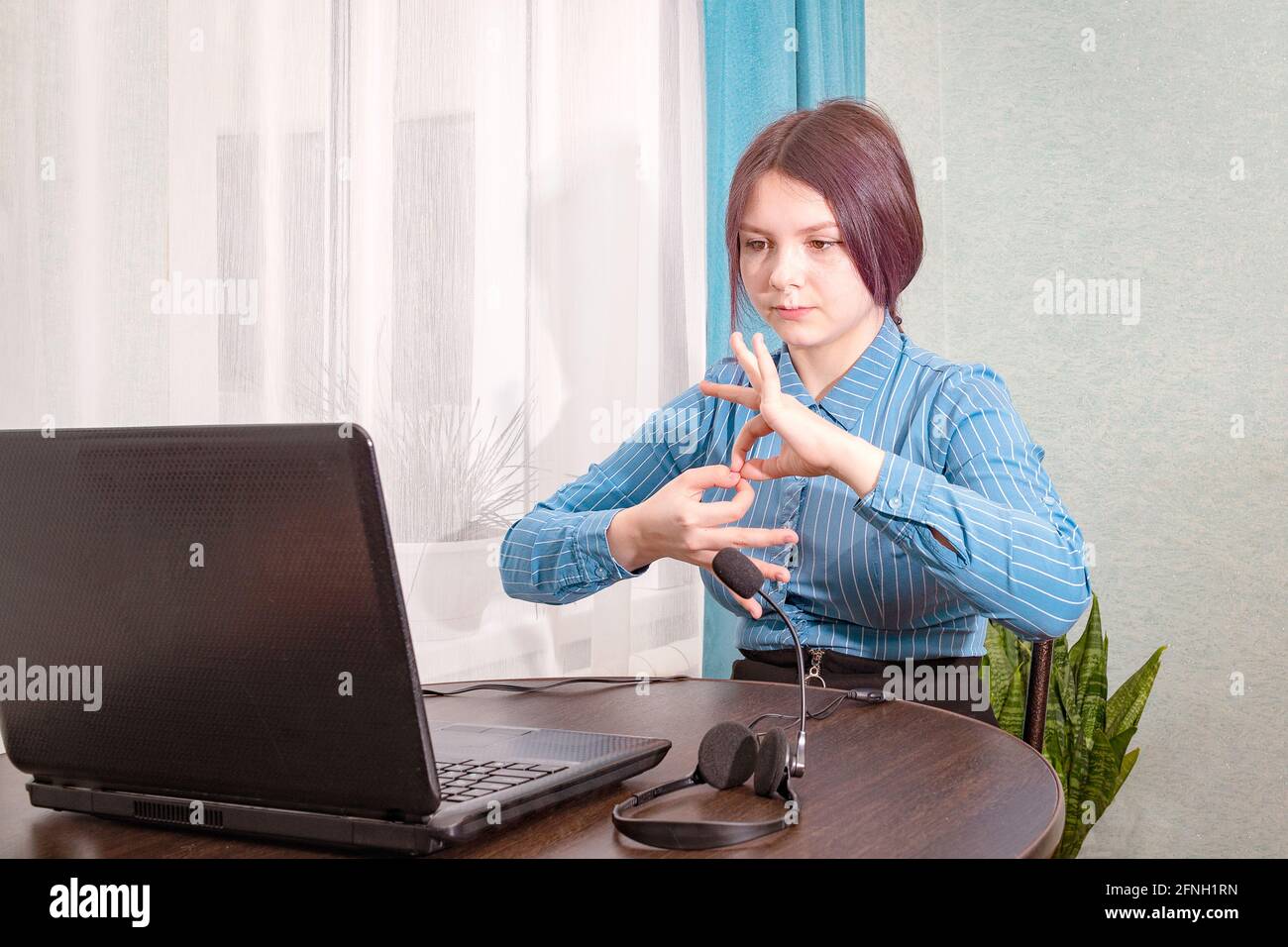 A teenage girl sits in front of her laptop learning sign language, a language for the deaf and dumb online Stock Photo