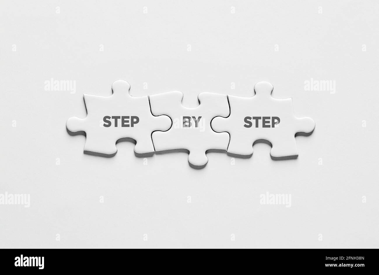 Achievement, progress or patience in business, career, education or learning. The message step by step on connected jigsaw puzzle pieces. Stock Photo