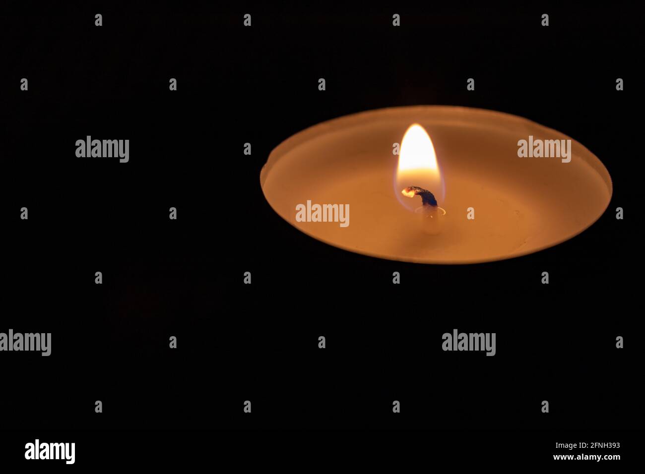 Single lit tealight candle against black background Stock Photo