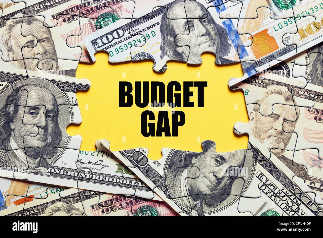 The word budget gap surrounded by puzzle pieces with dollar bill money. Business finance concept. Stock Photo