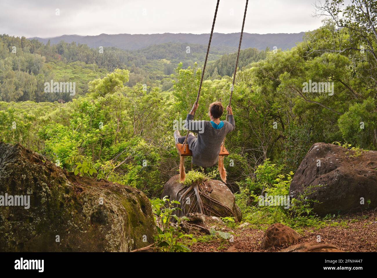 Woman sitting on rope swing hanging from tree, perched on hilltop of