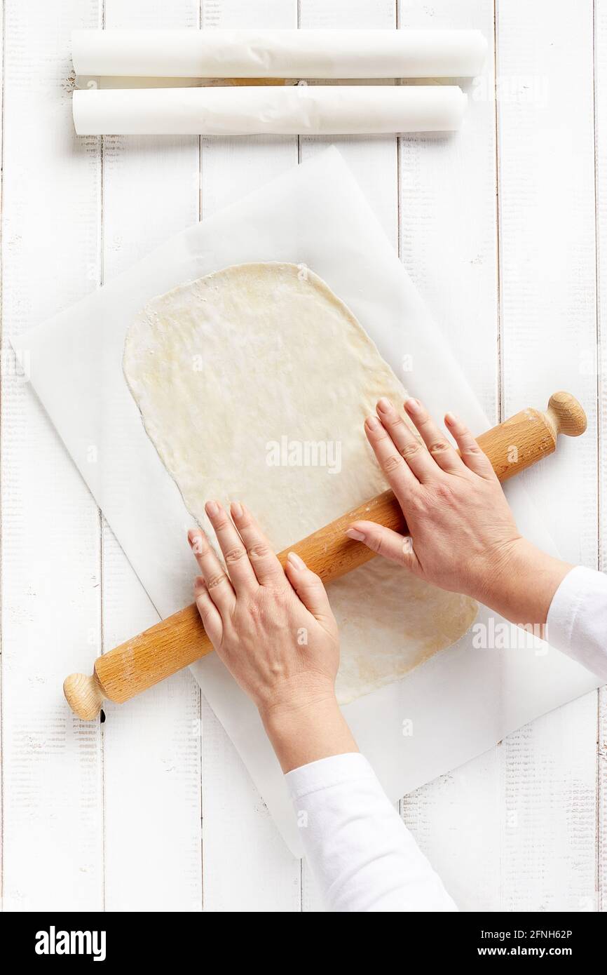 Woman hands spreading a very thin strudel dough with a rolling pin on a sheet of kitchen paper with cornstarch to prevent sticking Stock Photo