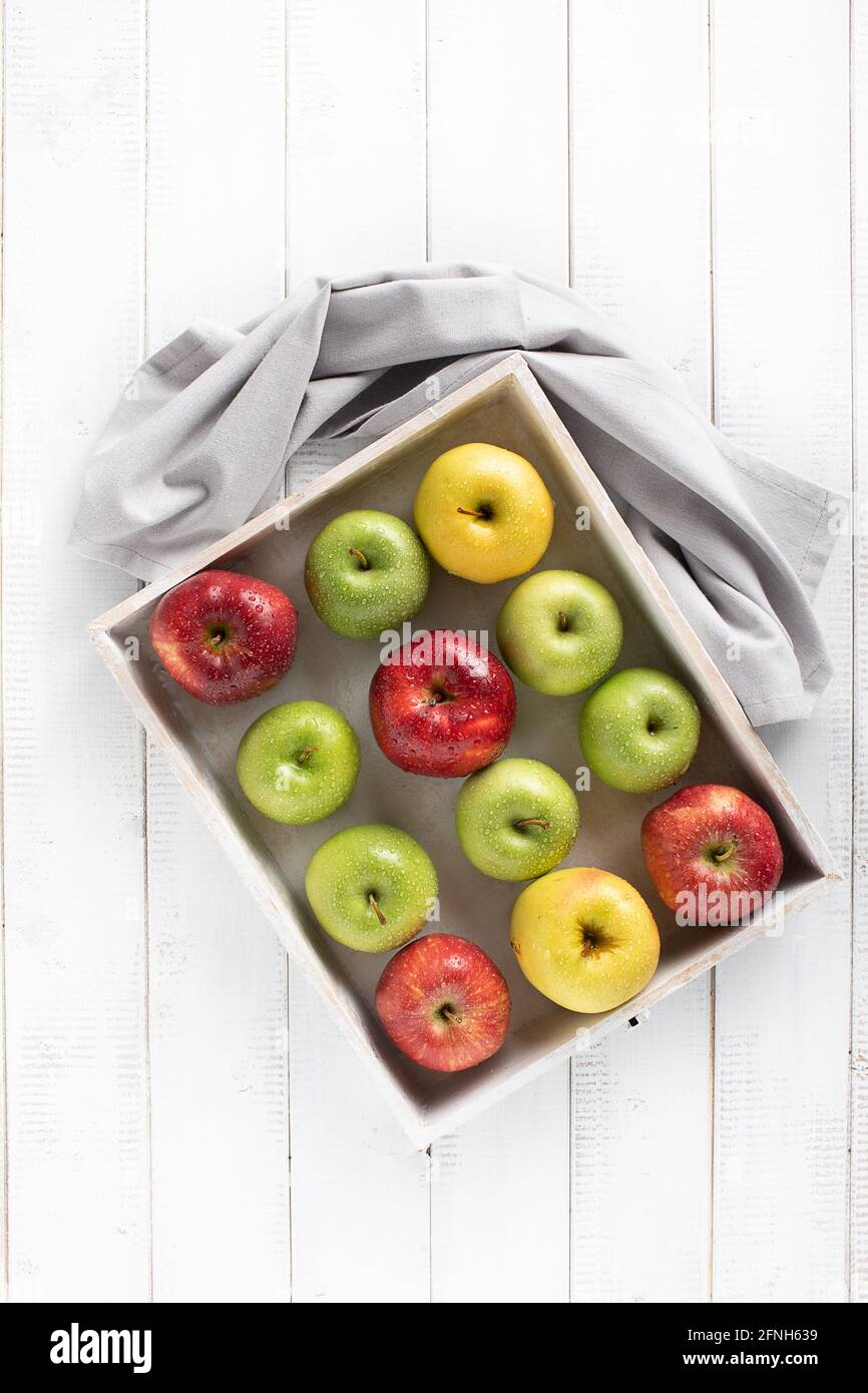 Colorful apples in a white wood tray on a white table top view Stock Photo