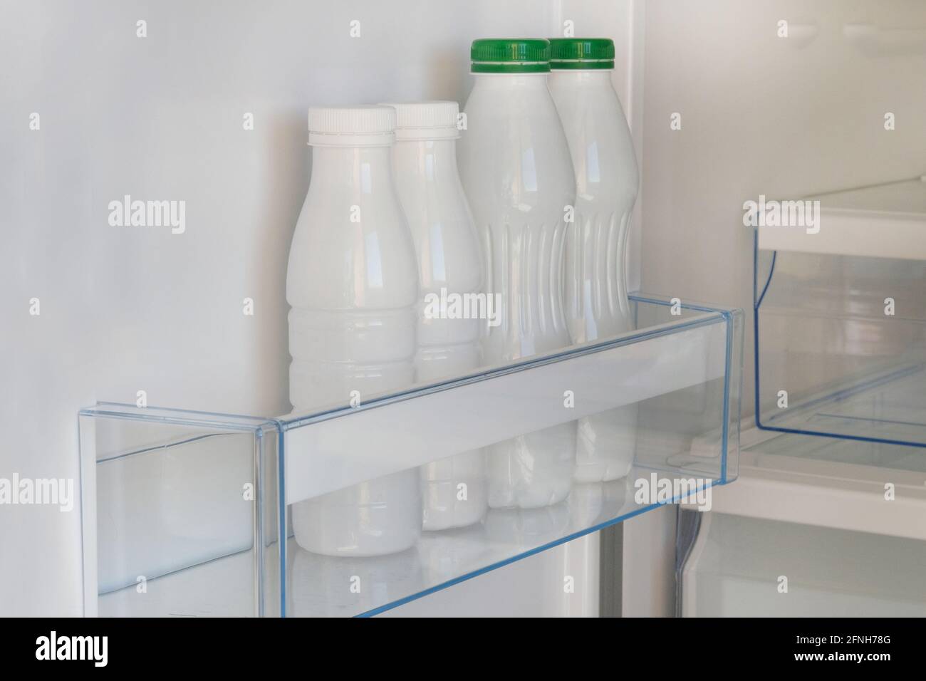Dairy products in in white plastic bottles on shelf of open empty fridge. White yoghurt in refrigerator. Fermented food. Stock Photo