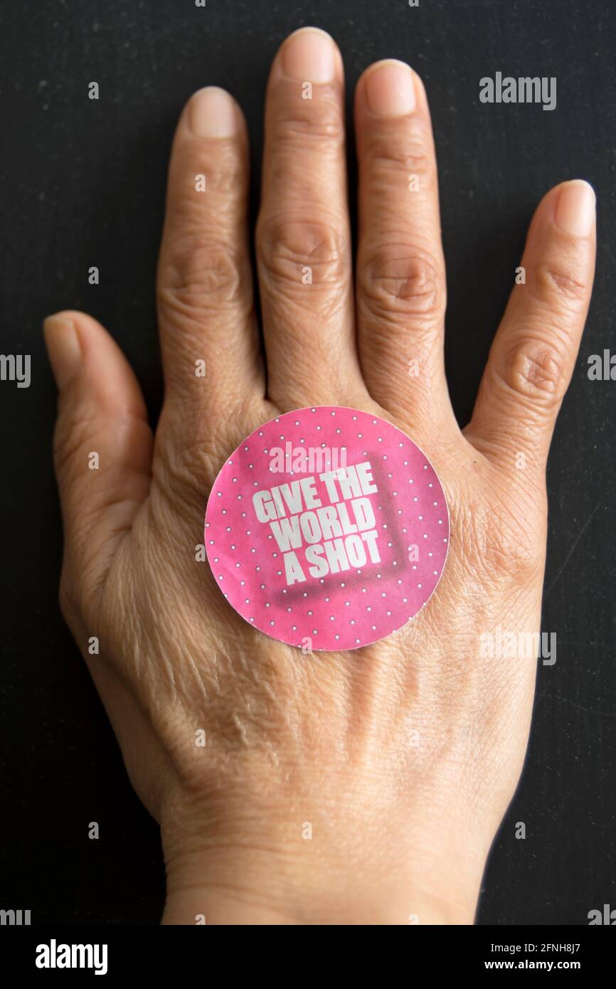on an asian female hand, a give the world a shot sticker advocating global rollout of the covid 19 vaccine Stock Photo