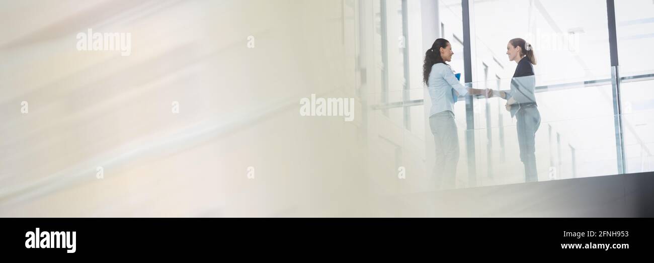 Two caucasian women having an handshake in front of to colleagues Stock Photo
