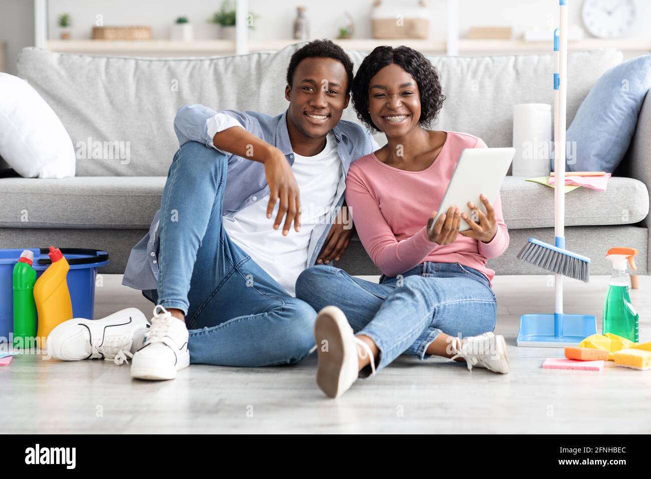 Black couple with cleaning tools resting, using digital tablet Stock Photo