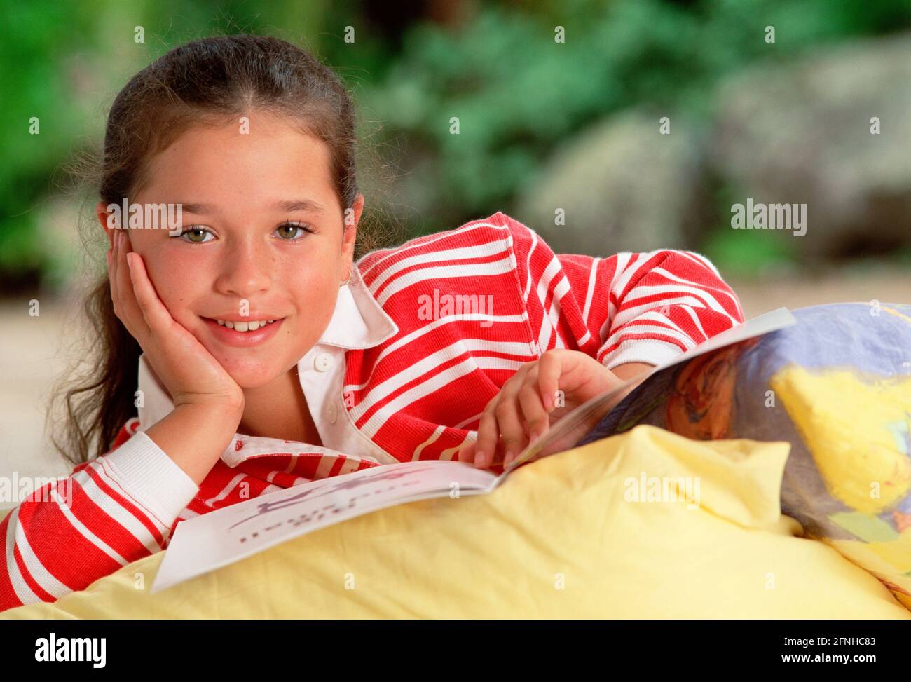 Lifestyle. Children. Girl at home reading while lying on pillows. Stock Photo