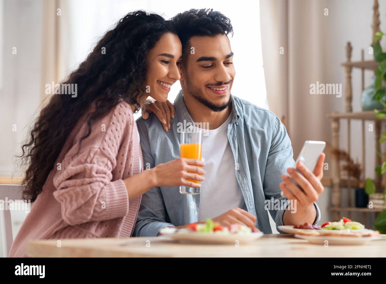 Happy Middle Eastern Couple Browsing Internet On Smartphone While Having Breakfast Stock Photo