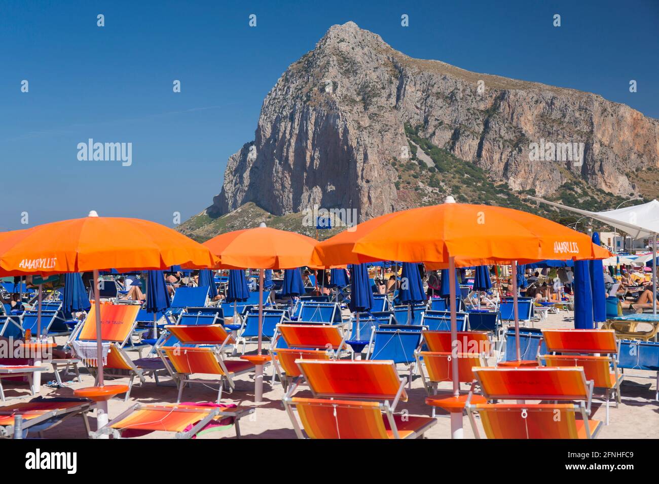 San Vito Lo Capo, Trapani, Sicily, Italy. View along crowded shore to the towering north face of Monte Monaco, striking beach furniture in foreground. Stock Photo