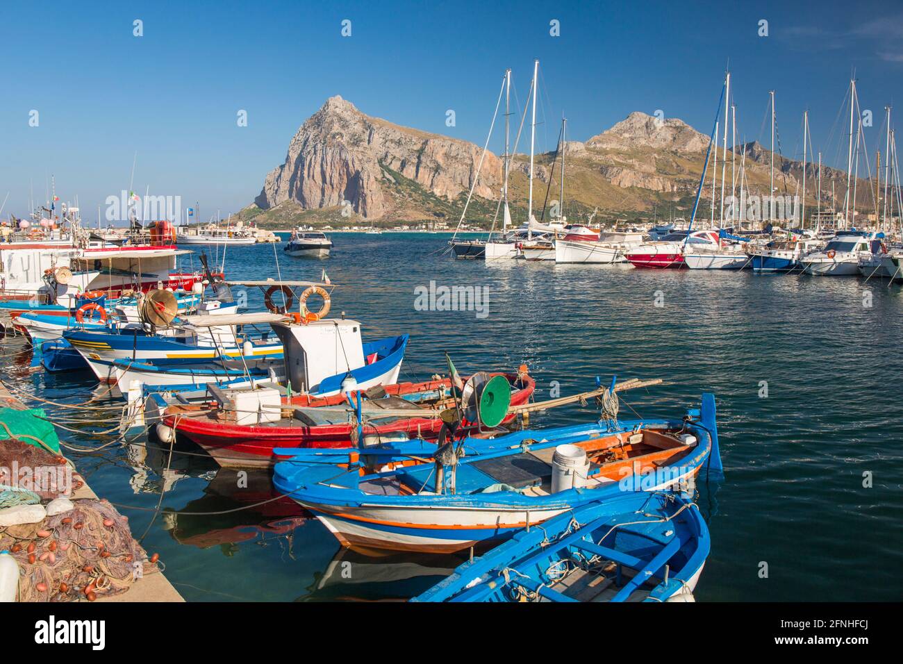San Vito Lo Capo, Trapani, Sicily, Italy. View across colourful harbour to the towering peaks of Monte Monaco and Pizzo di Sella. Stock Photo