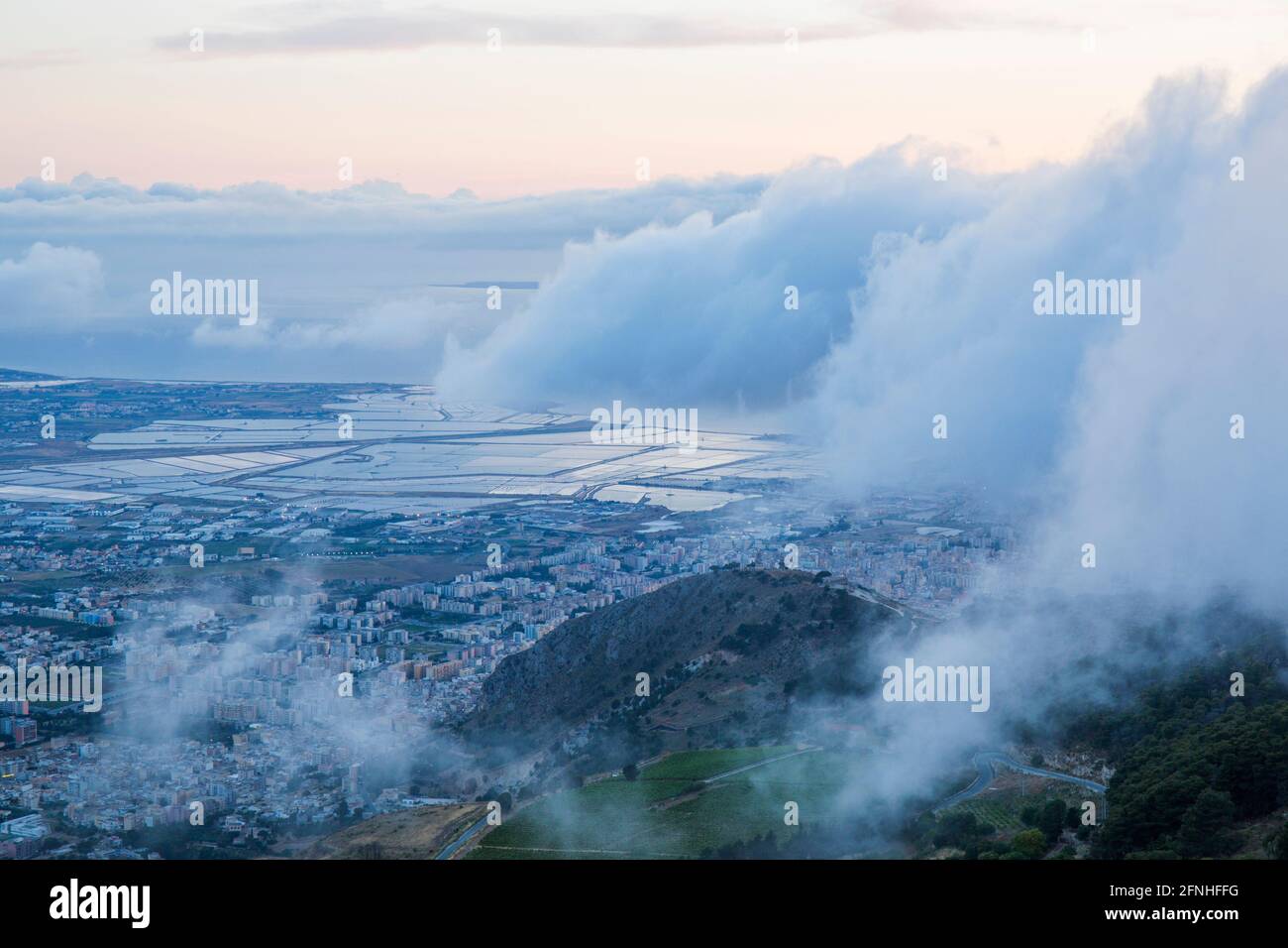 Erice, Trapani, Sicily, Italy. View over the Trapani salt flats from the summit of Monte Erice, dusk, low clouds drifting across hillside. Stock Photo