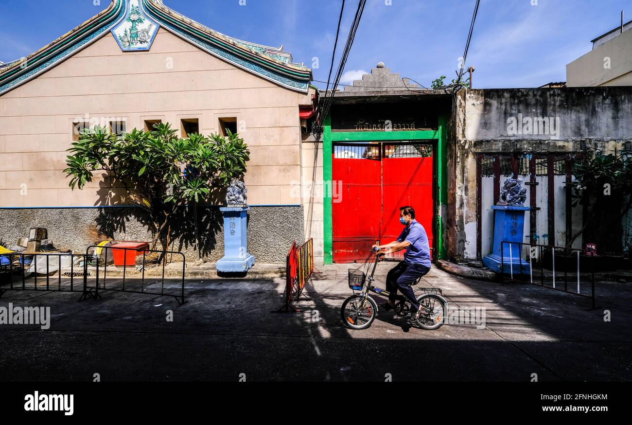 A man cycles past the entrance to Wat Mangkon in the Chinatown area of Bangkok, Thailand Stock Photo