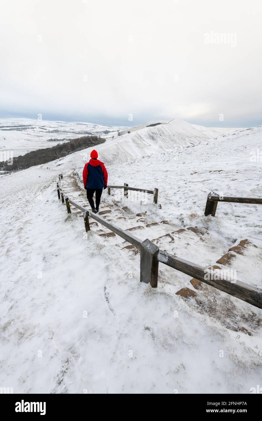 Male in red coat in winter walking towards Rushup Edge from Mam Tor, Peak District, Derbyshire Stock Photo