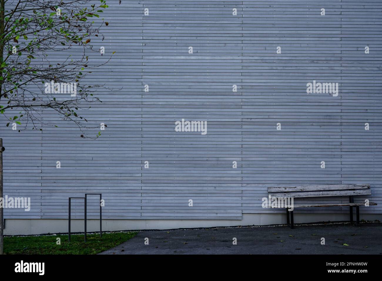 View of a house wall in front of which there is a wooden bench and a bicycle stand. Stock Photo
