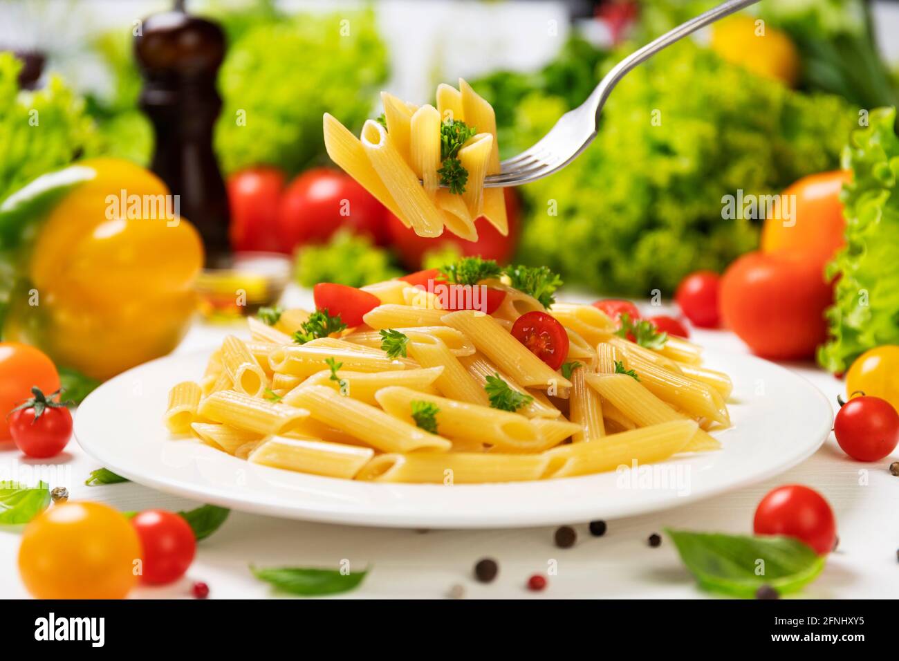 Plate of italian pasta, penne rigate on fork with tomatoes and basil Stock Photo