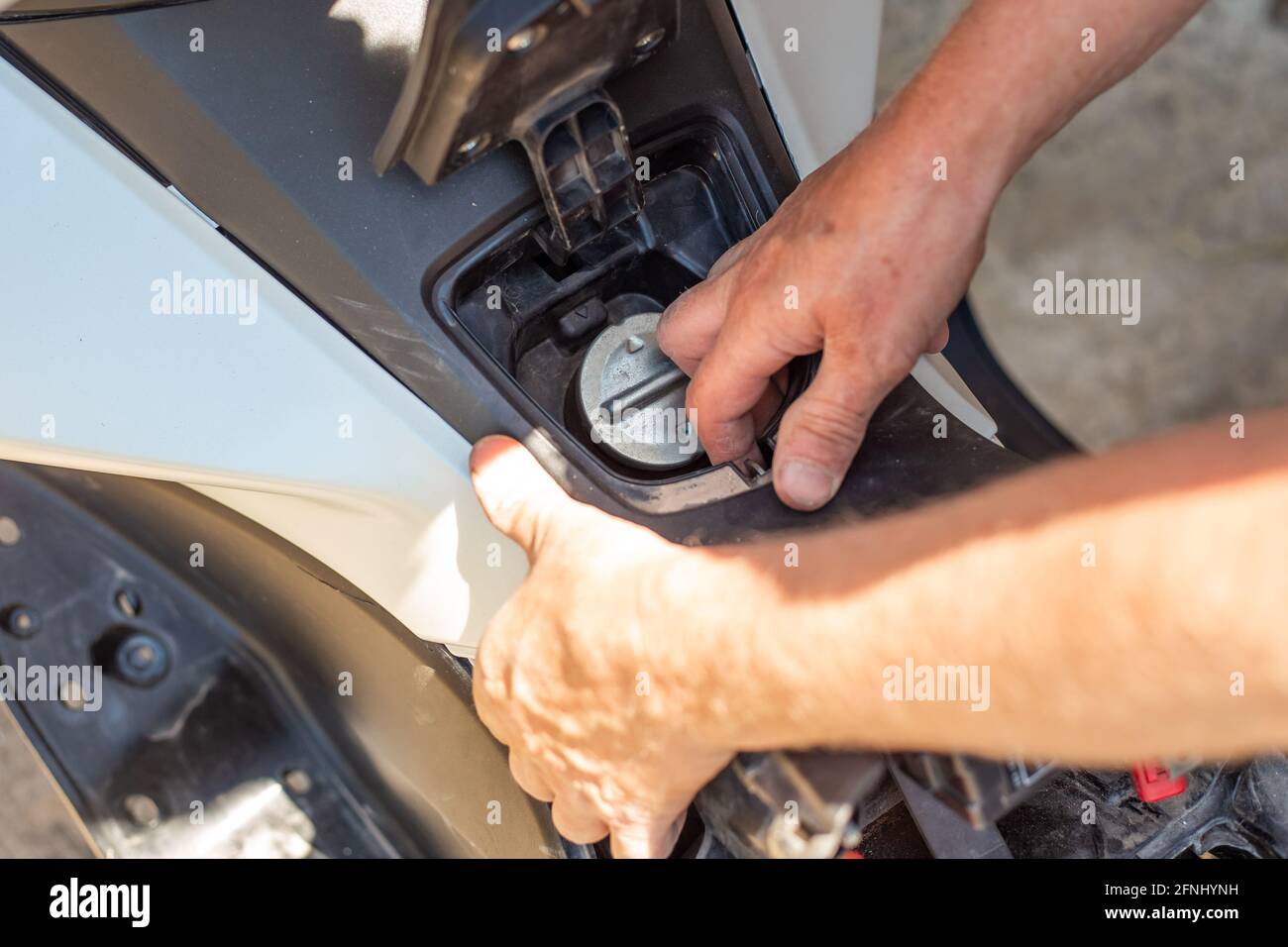 The man opened the gas tank flap for refueling the motorbike with gasoline. Maintenance of
