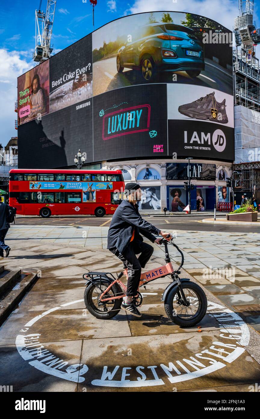 London, UK. 17th May, 2021. A Mate electric bike passes - On the day Cinemas are allowed to re-open, a 3-D live action billboard, Piccadilly Lights, to launch Zack Snyder's (Justice League) forthcoming blockbuster movie ARMY OF THE DEAD. Credit: Guy Bell/Alamy Live News Stock Photo