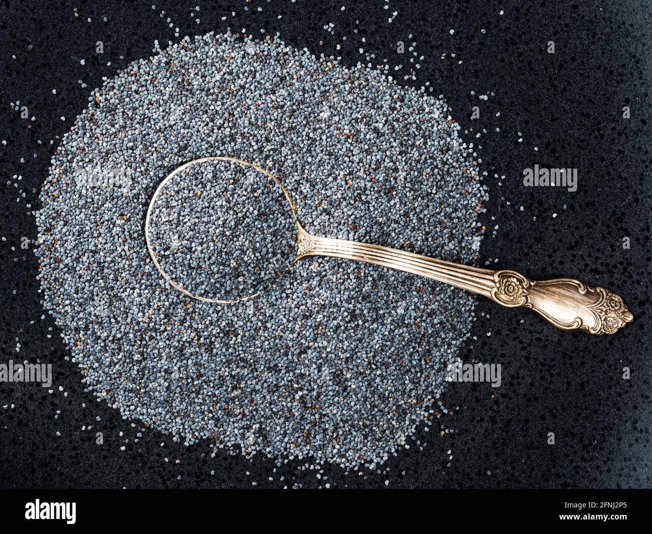 top view of silver tablespoon in poppy seeds on black plate Stock Photo