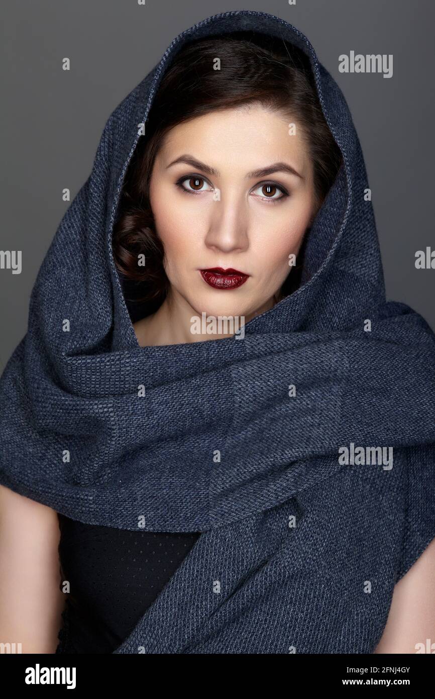Beauty portrait of brunette woman dressed in dark blue scarf. Female portrait from a three-quarter angle on black background. Stock Photo