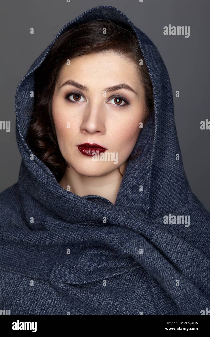 Beauty portrait of brunette woman dressed in dark blue scarf. Female portrait from a three-quarter angle on black background. Stock Photo