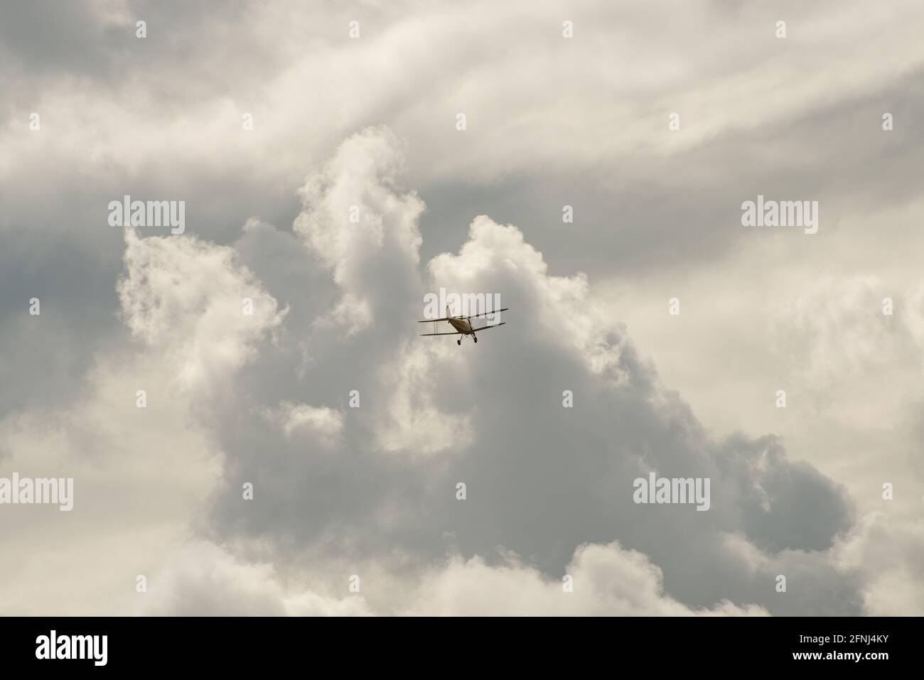 Small biplane high in the air flying towards a bank of clouds towering in front of and above it Stock Photo