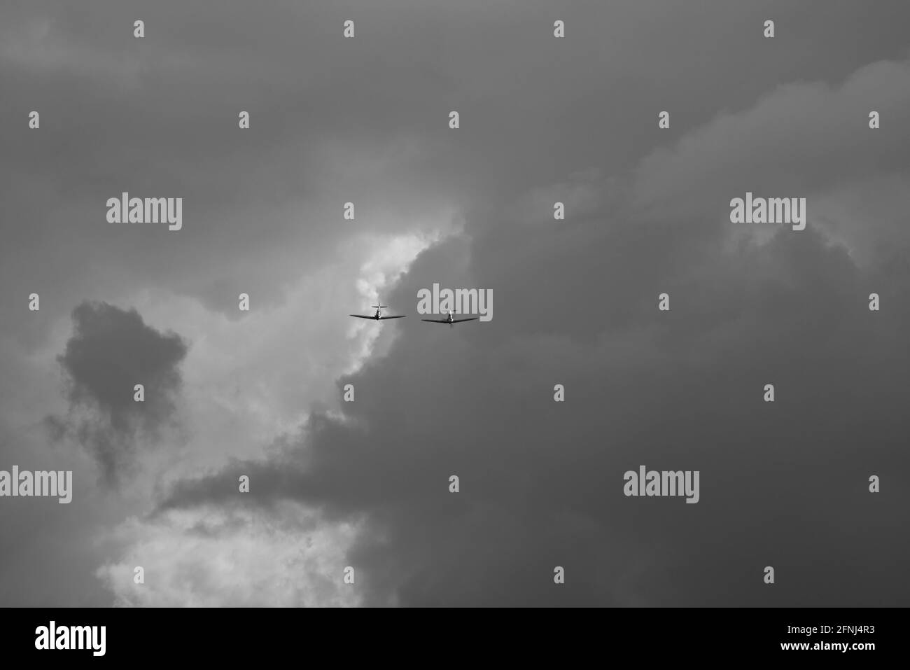 Mono image of two Spitfire fighters wing to wing coming out of the clouds and heading towards the viewer Stock Photo