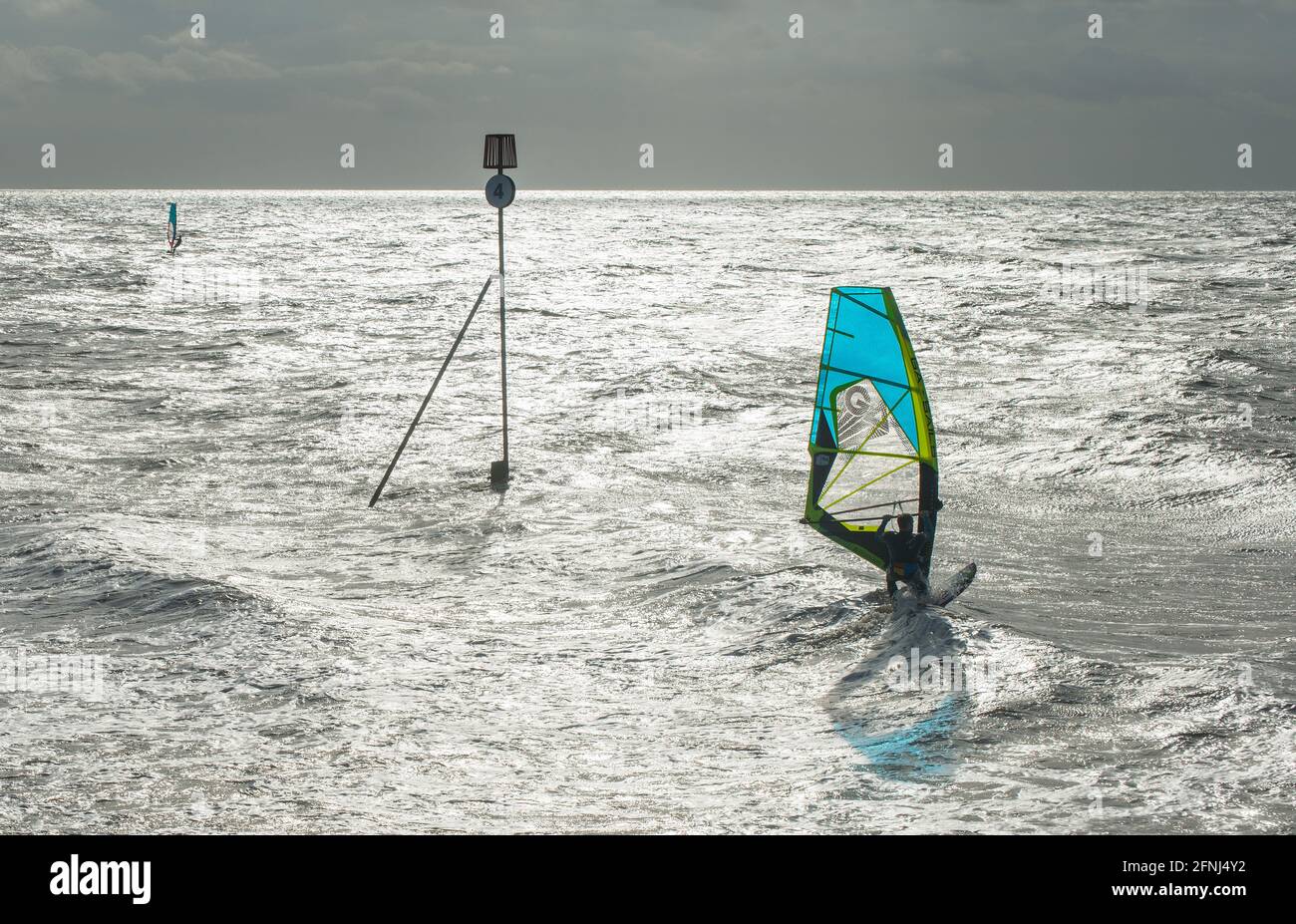 Spectacular image of two windsurfers skimming across a silvery sea with their colourful sails reflected on the water and a dark sky horizon backdrop Stock Photo