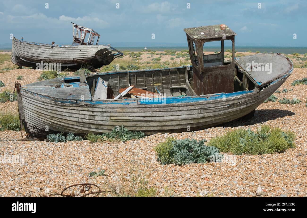 Colour image of two rotting fishing boats high on a gravel shore each keeling over to one side Stock Photo