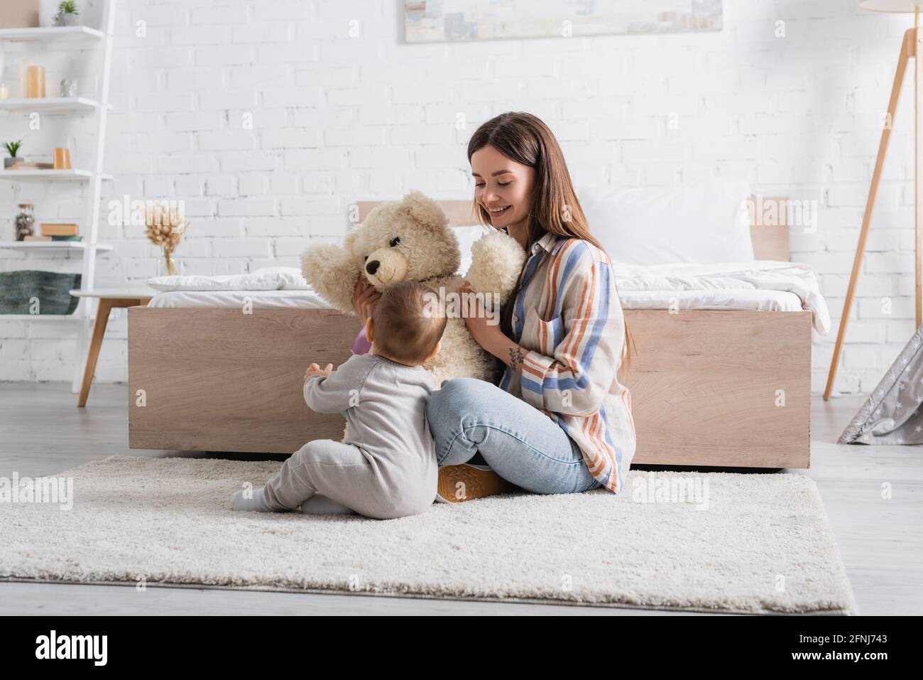 tattooed young mother holding teddy bear near infant son Stock Photo