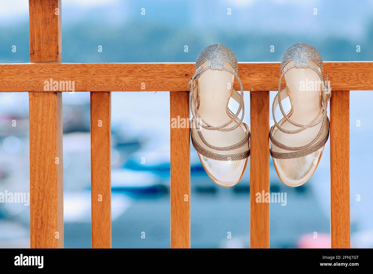 Bride’s gold heeled sandals hanging on a wooden railing against a blue