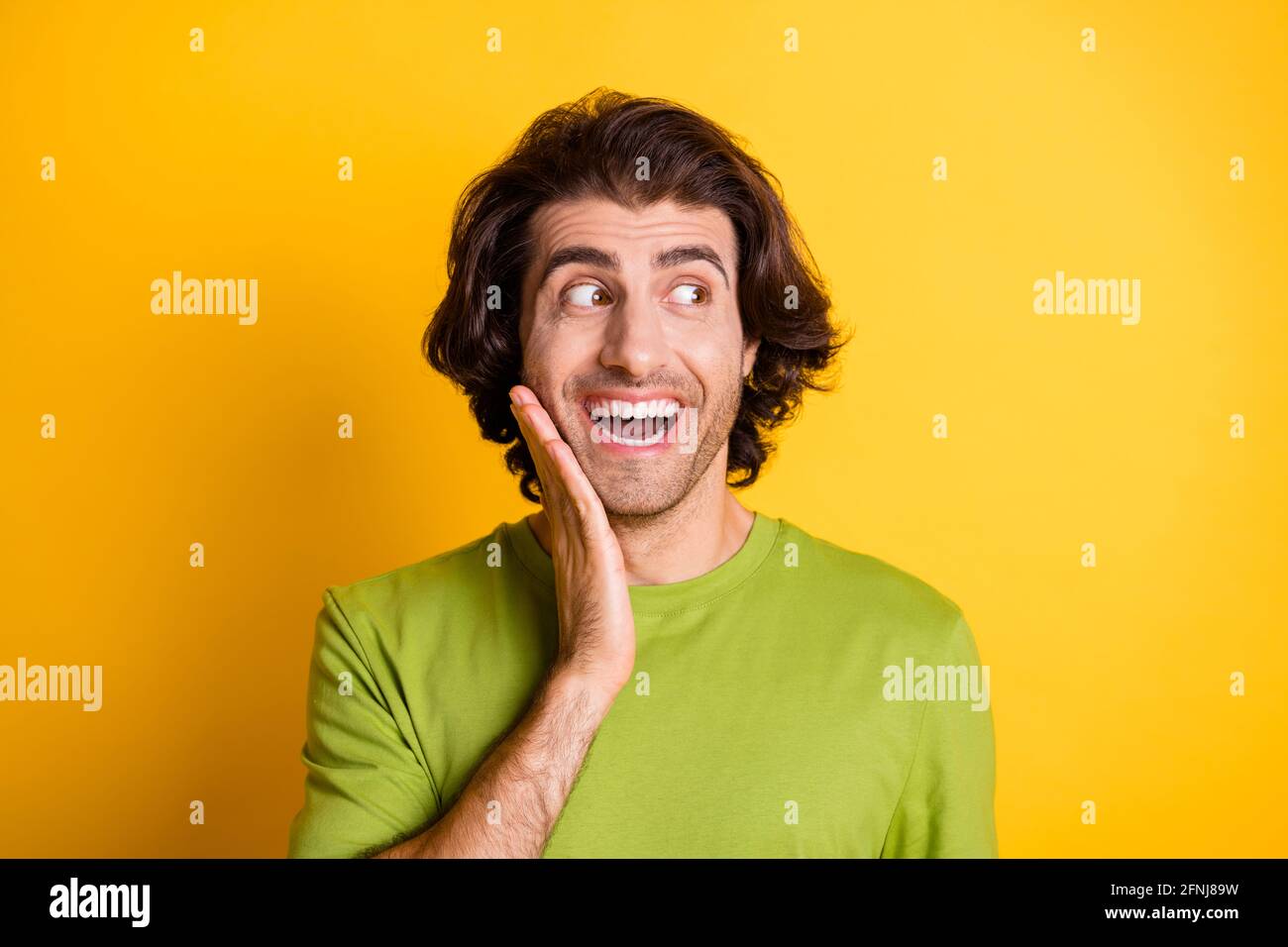Photo of funky crazy guy palm cheekbone look side empty space wear green t-shirt isolated yellow color background Stock Photo