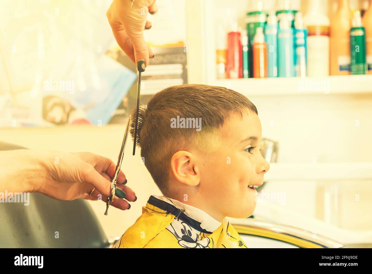 little boy having a haircut at hair salon..Children hairdresser with scissors and comb is cutting little boy. Contented cute preschooler boy getting Stock Photo