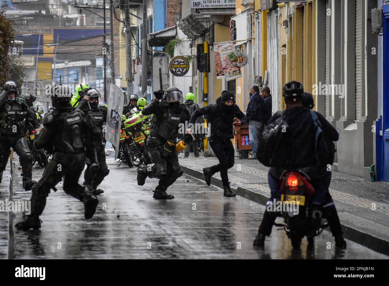 Riot police members chase demonstrators after clashes around the national strike in Pasto Narino on May 1, 2021. Riot police runs to return tear gas grenade to demonstrators in Pasto Narino on May 1, 2021. During the demonstrations against the tax reform of president Ivan Duque Marquez Stock Photo