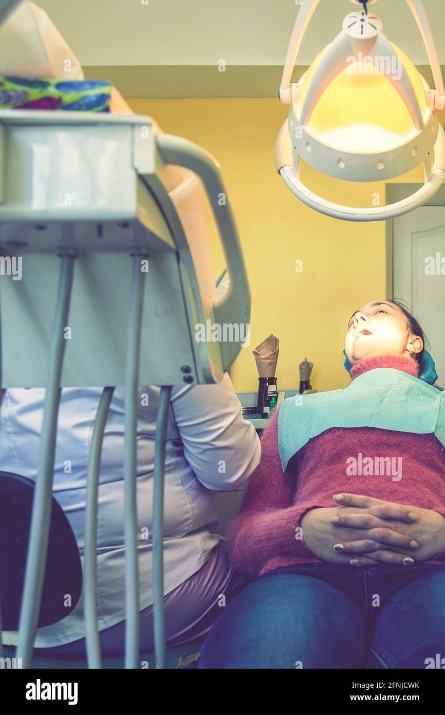 Male dentists examining and working on young female patient.Dentist's office. Real woman in a chair at the dentist. vertical photo. toned Stock Photo