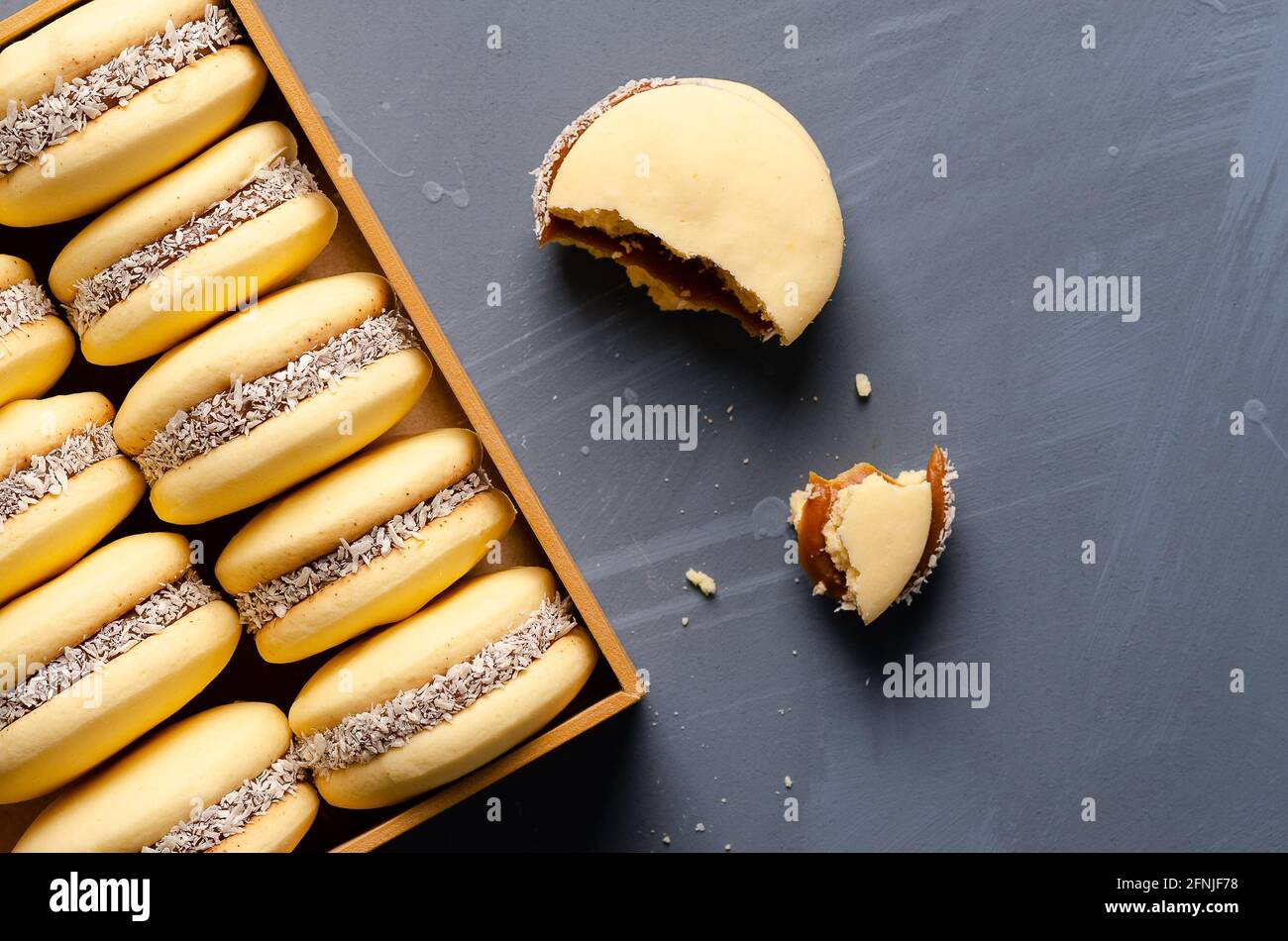 Cornstarch alfajores with milk caramel and coconut in a wooden box on a light blue background. Stock Photo