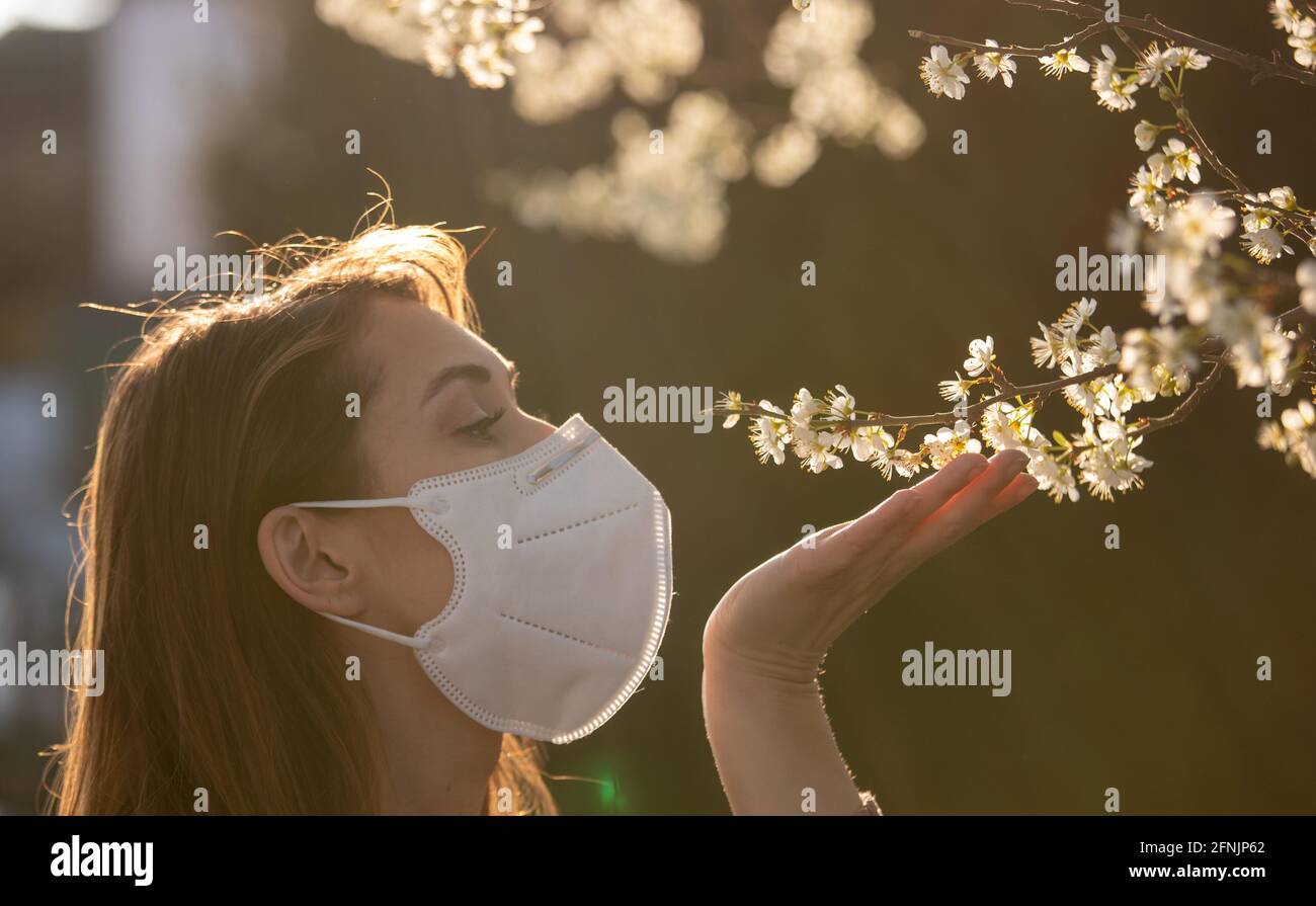 Pretty young girl with facial mask smelling blooming tree. Spring