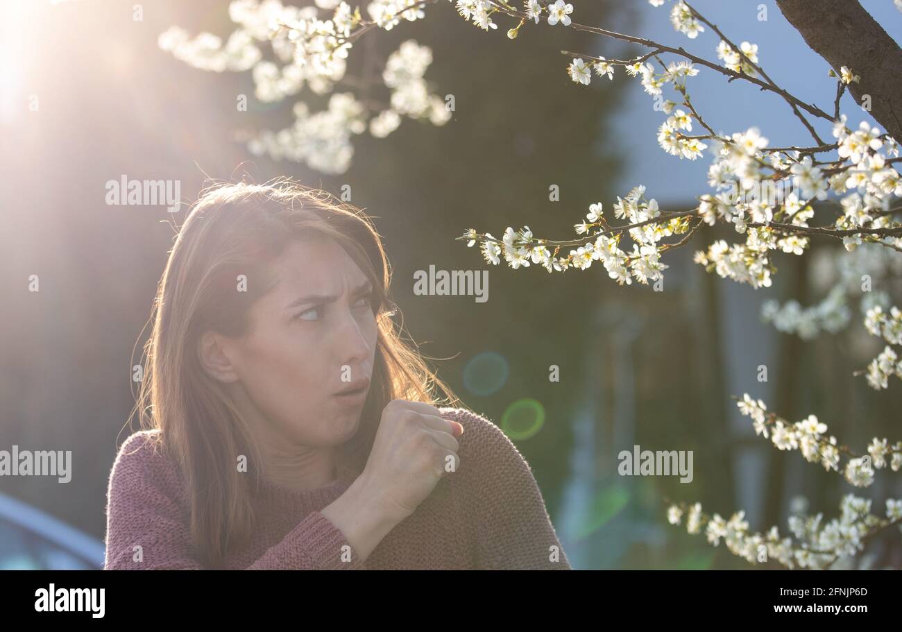 Pretty young girl coughing in front of blooming tree. Spring allergy