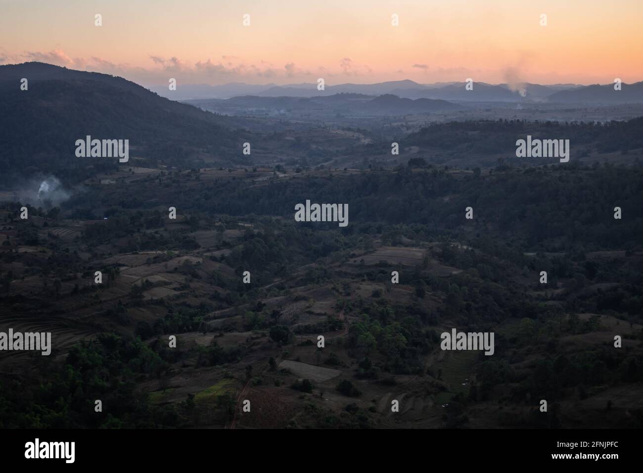 Orange sunset from a viewpoint looking out over the farm lands and hills underneath in a valley between Kalaw and Inle Lake, Shan state, Myanmar Stock Photo