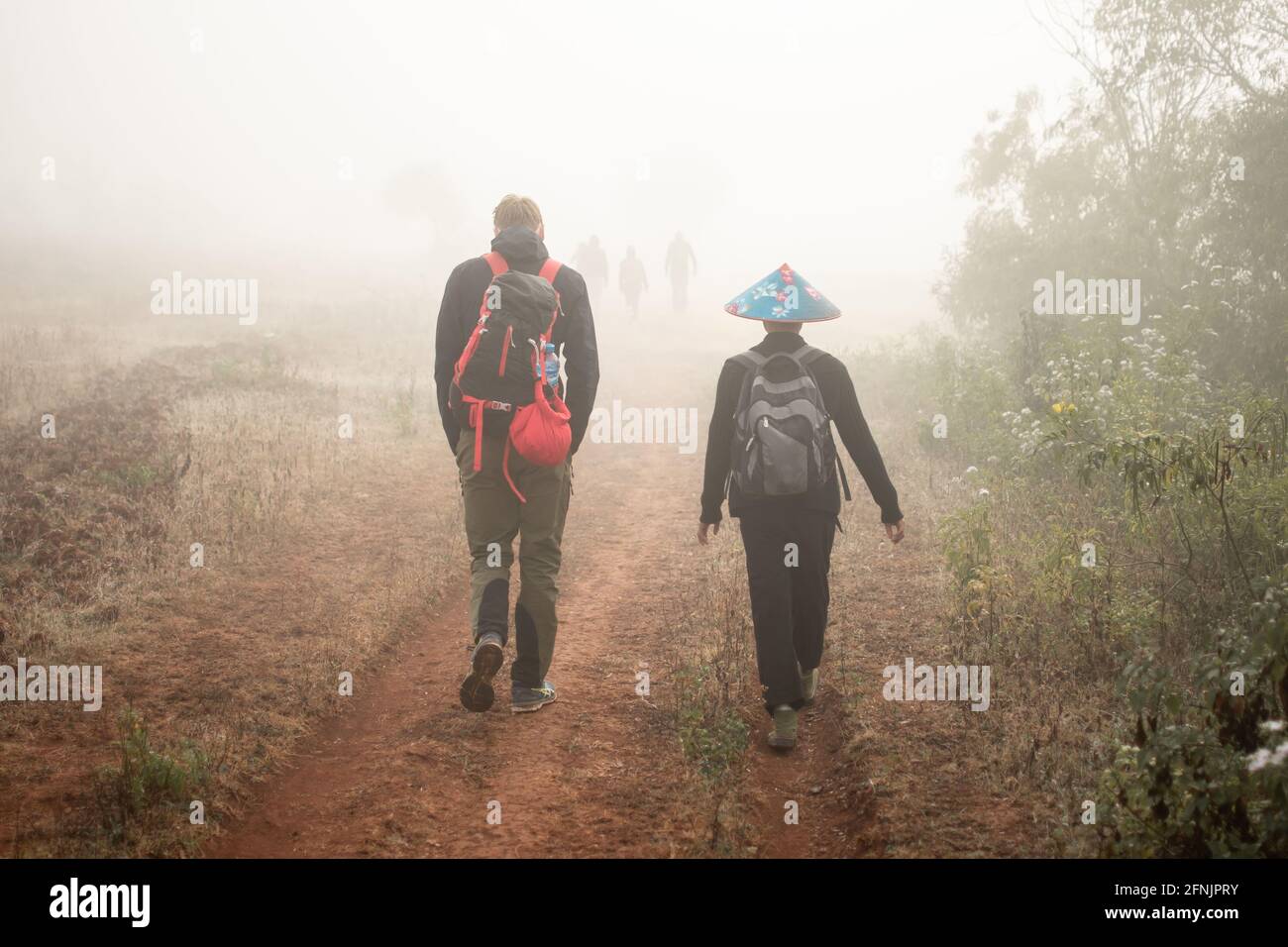 People walking away in heavy early morning mist and fog on a hike from Kalaw to Inle Lake, Shan state, Myanmar Stock Photo