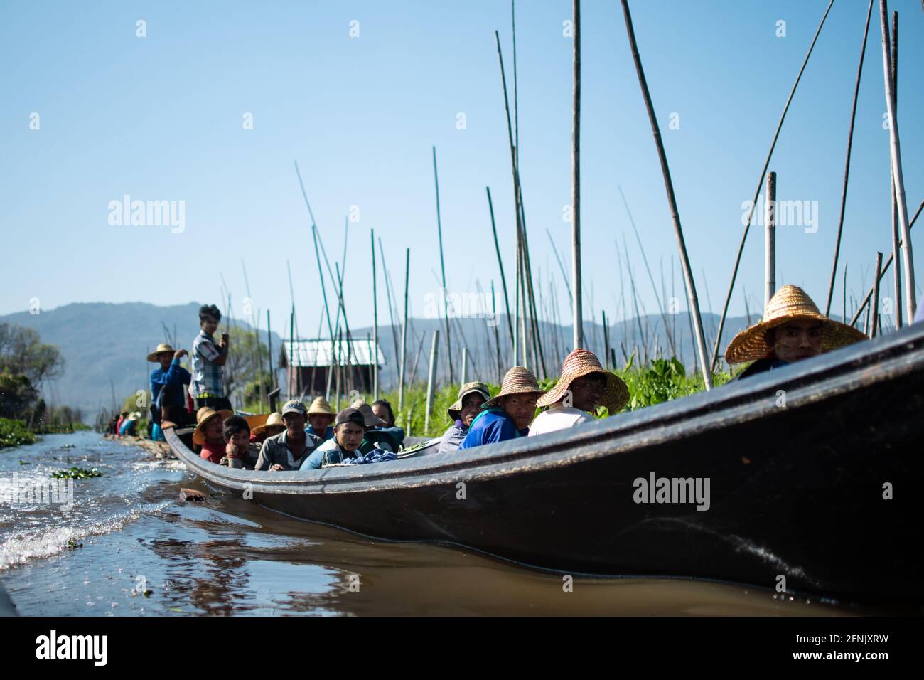 Shan state, Myanmar - January 7 2020: Locals travels by traditional boat past the floating gardens in a canal by Inle Lake, Nyaung Shwe Stock Photo
