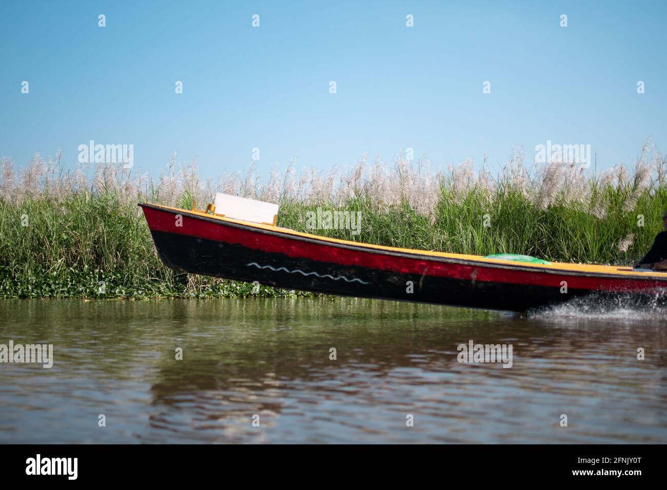 The front of a traditional red and black wooden boat above water level in high speed by the floating gardens of Inle Lake, Nyaung Shwe, Myanmar Stock Photo