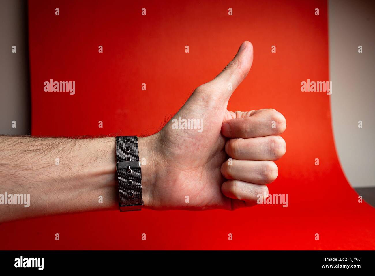 Men's hand with watch shows thumb on red background Stock Photo