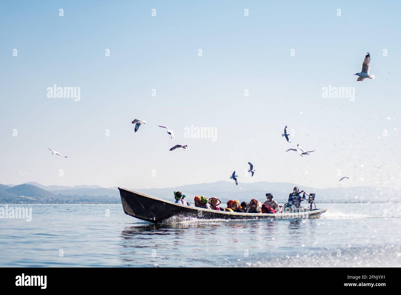 Inle Lake, Nyaung Shwe, Shan state, Myanmar - January 7 2020: Locals travels by traditional boat with birds above and mountains in the background Stock Photo
