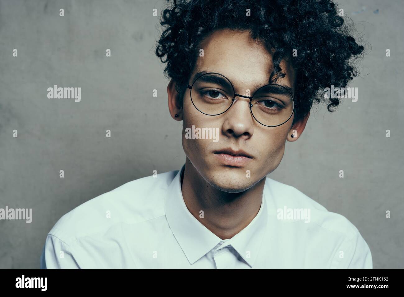 portrait of a nice guy with curly hair on a gray background and a light  shirt glasses model close-up Stock Photo - Alamy