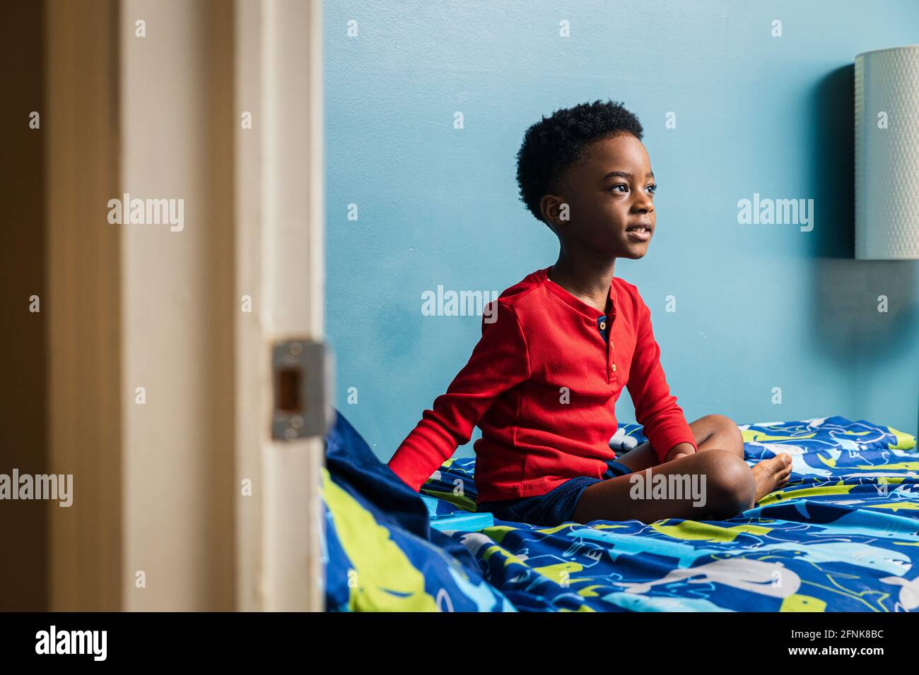 Thoughtful boy looking away while sitting on bed at home Stock Photo