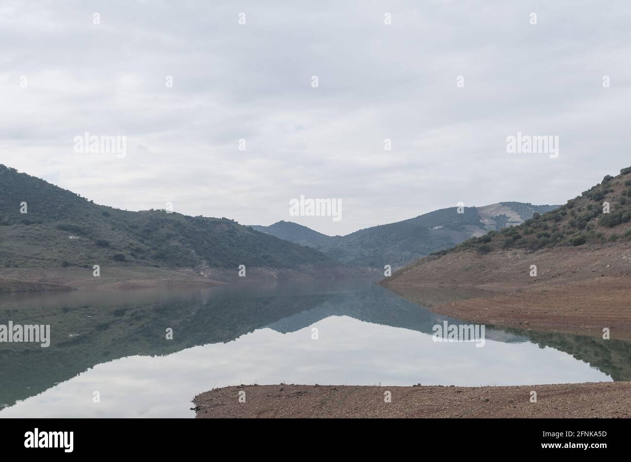 Stunning view of hills reflected on a tranquil mirror-like lake on a rainy day under a cloudy sky Stock Photo