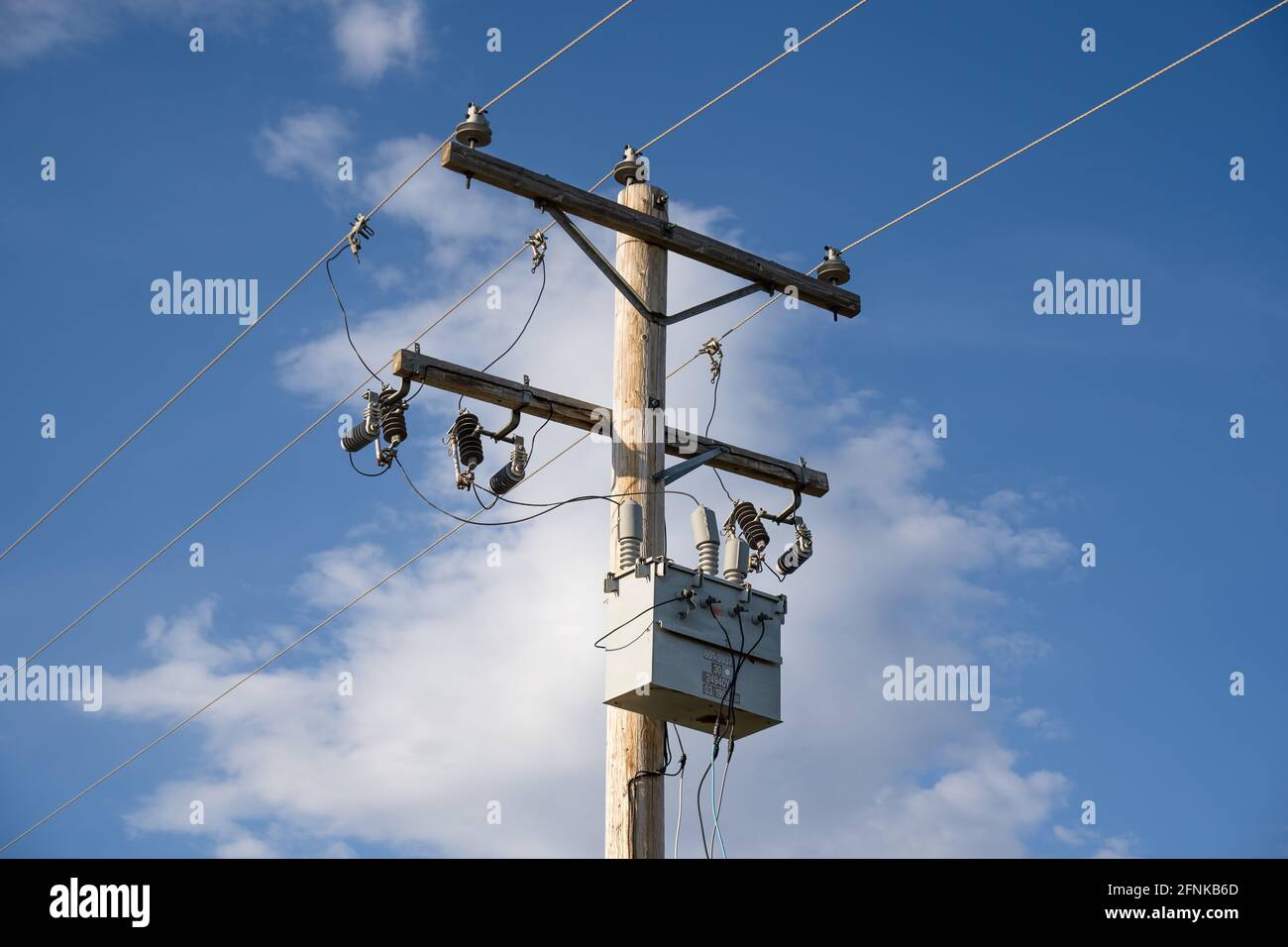 A wooden power pole and transformer with communication and transmission lines under a blue sky background. Stock Photo