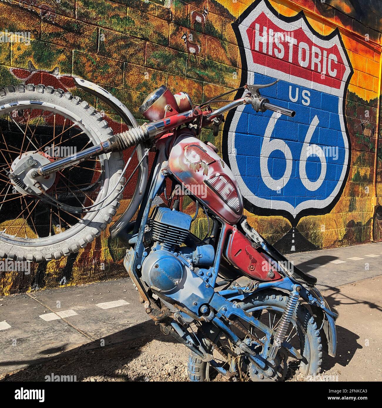 A colourful painted Kawasaki Motorcycle artwork piece partially embedded in the ground in front of a bright colourful wall with a historic US Route 66 Stock Photo