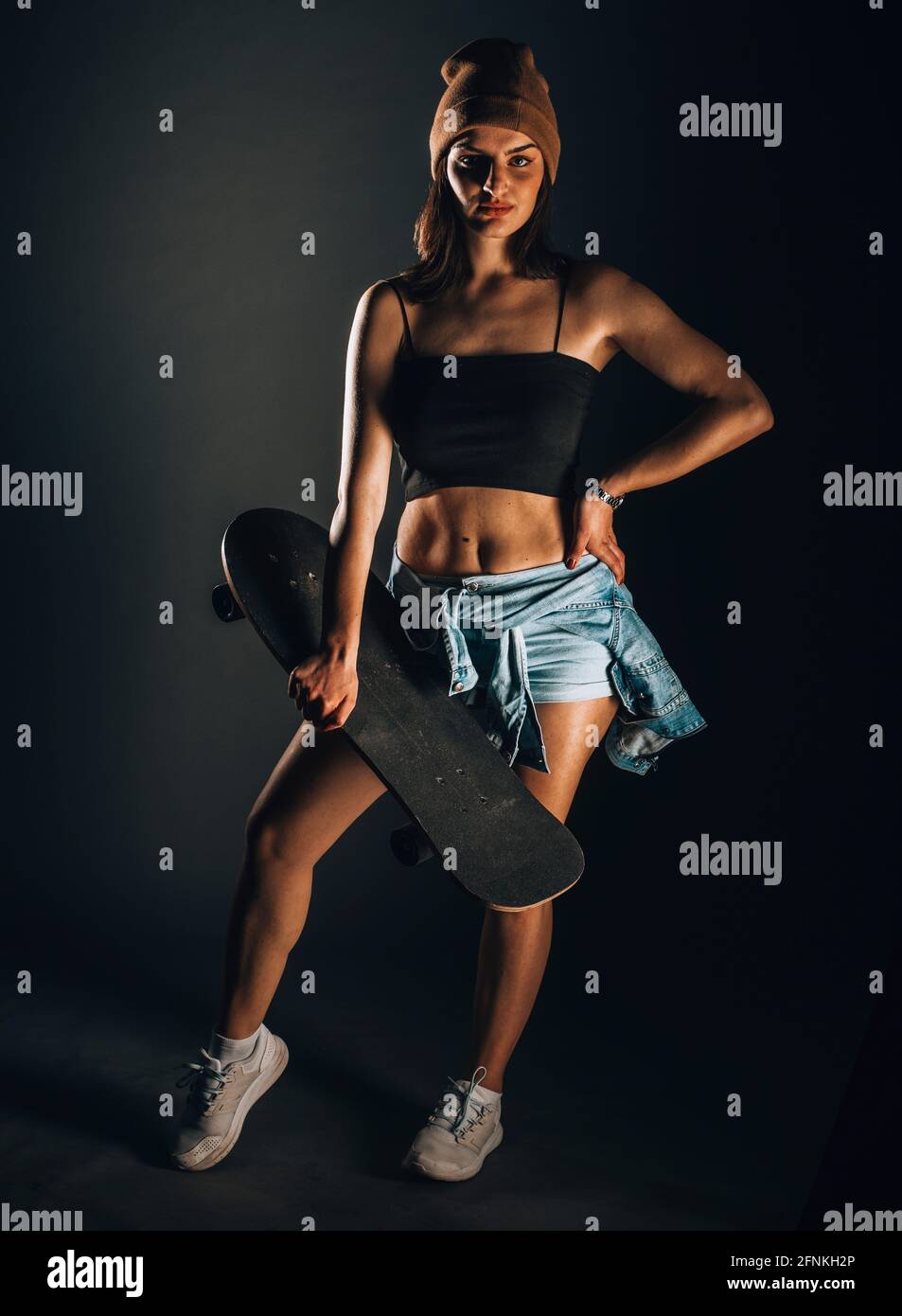 Portrait of an attractive trendy girl in black tank top and ripped jeans  posing against dark wall Stock Photo - Alamy